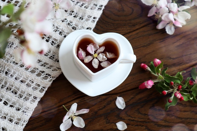 봄 티 파티는 사과 나무 꼭대기의 꽃 가지 사이에서 나무 배경에 하트 모양의 차 한 잔을 제공합니다.
