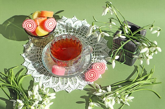 Spring tea party a cup of tea with pink marmalade bouquets of snowdrops around white lace doily pastel background top view