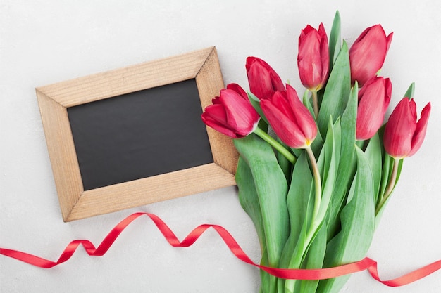 Spring tulip flowers with ribbon and wooden frame with empty space for text on gray stone table top