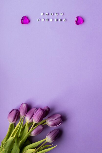 Spring tulip and text happy birhday on english laid out of multi-colored cube on violet background