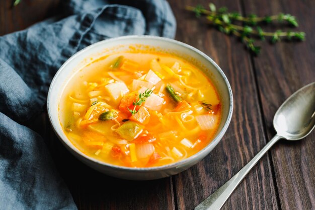 Zuppa di verdure primaverili con brodo di pollo per una persona su tavola di legno vista in primo piano in stile rustico