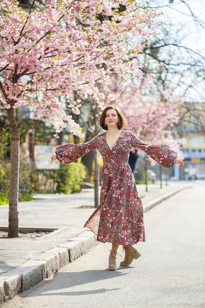 春になると、桜の木が咲き乱れる通りを女性が歩きます。長いシルクのエレガントなヴィンテージドレスを着た女の子が花の木々の間を歩きます