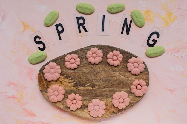 Photo spring word and flower cookies on a wooden board on a pink background spring holidays cooking concept