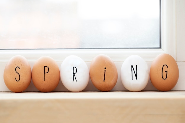 Primavera scritta sulle uova sullo scaffale di legno, sul fondo di concetto della primavera o di pasqua con luce solare