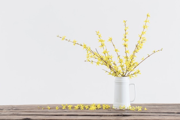 Spring yellow flowers in white jug on white surface