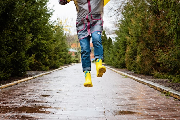 Springen in plas Vrouwelijke benen in gele rubberen laarzen springen op de plas Zorgeloos jonge vrouw in regenlaarzen springt