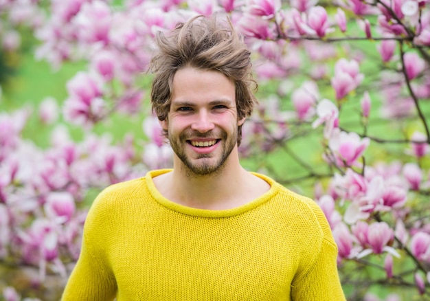 春のコンセプト。男の花の背景の焦点がぼけています。春の美しさ。春のシーズン。植物学と自然。幸せな春のコンセプト。流行に敏感な人は花の香りを楽しんでいます。無精ひげを生やした男がマグノリアの花を嗅ぎます。