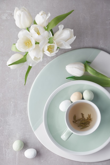 Springtime flat lay in pastel colors, white tulips and sugar Easter eggs on light stone