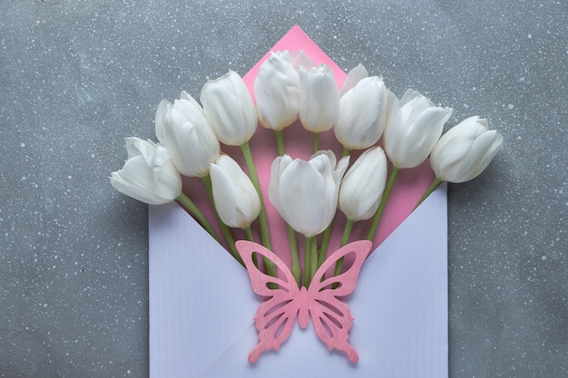 Springtime flat lay, white tulips in white and pink envelope on grey textured   