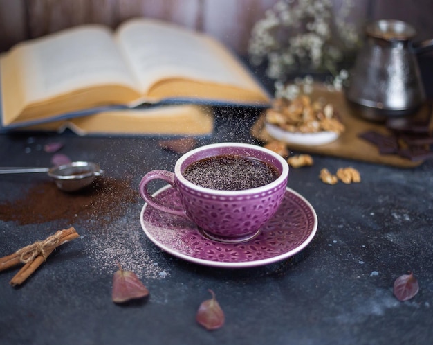 Фото Посыпать горячий кофе на темном деревянном фоне с открытыми книгами порошком корицы