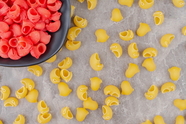 Sprinkled pipe pasta and a bowl of red pipe pasta, on the marble.