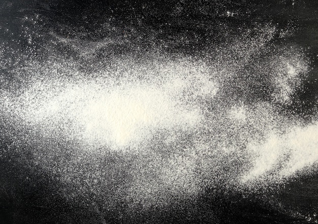 Foto farina bianca spruzzata sulla tavola nera, vista superiore