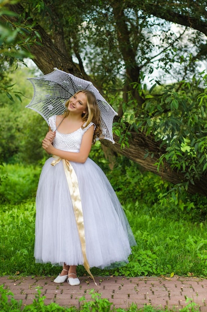 Sprookjesachtige ballerina in een prachtige jurk met een decoratieve paraplu komt uit het bos