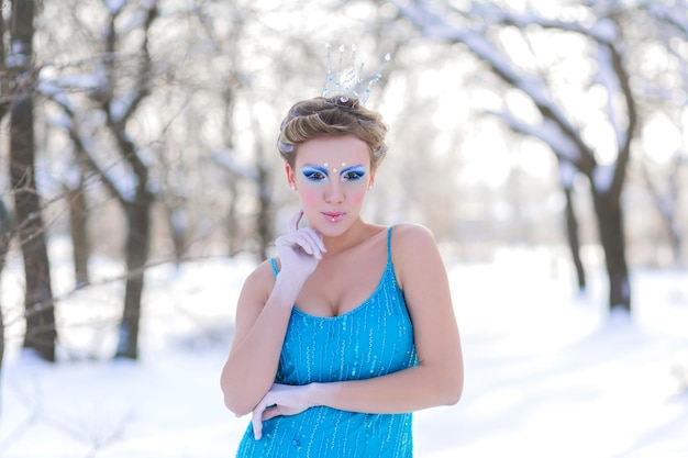 Sprookjesachtige cosplay van ijskoningin Vrouw in de jurk poserend in het besneeuwde bos