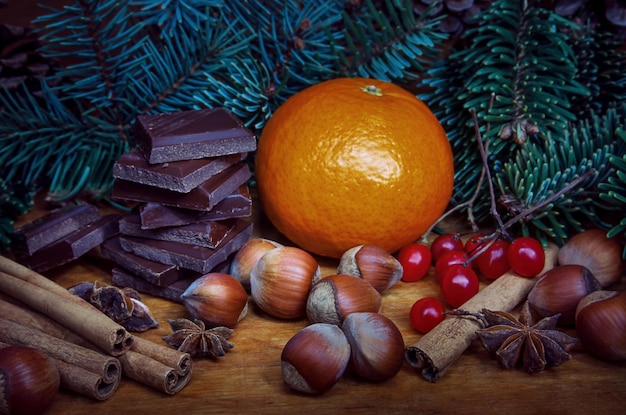 Spruce branches tangerine nuts cinnamon and chocolate lying on wooden background