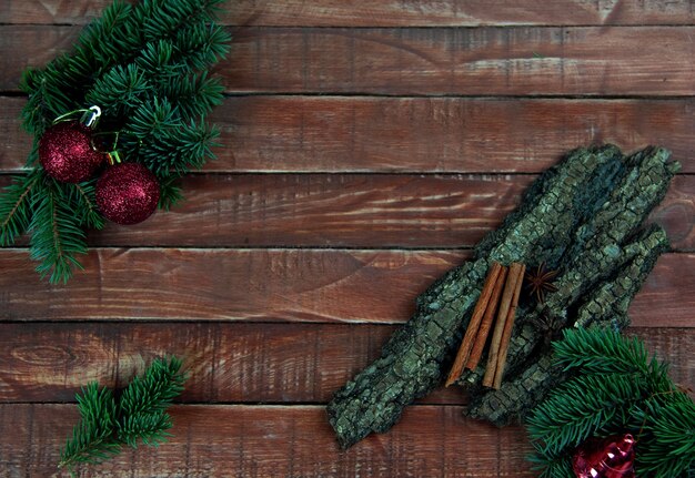 赤いクリスマスの装飾が施されたトウヒの枝は、樹皮とシナモンの棒で茶色の木の板の上にあります