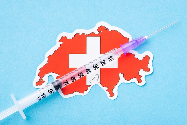 Spuit op de vlag van Zwitserland op blauwe achtergrond. Concept van succesvolle coronavirusvaccinatie in Zwitserland