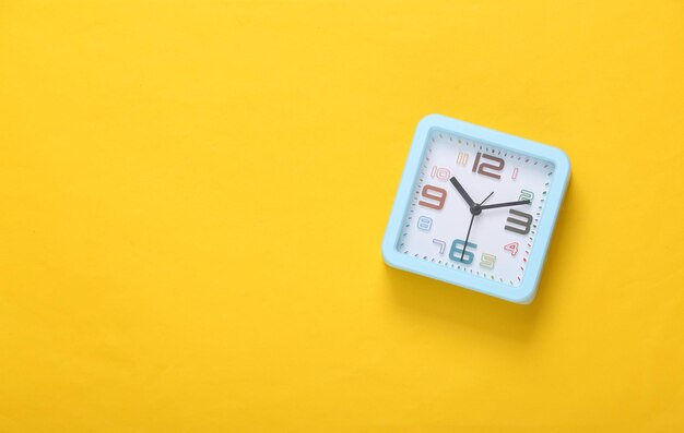 Square alarm clock on yellow background Top view