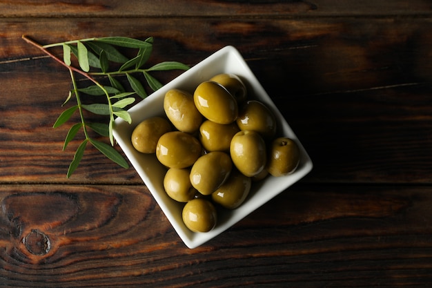 square bowl with olives and leaves on wooden, top view
