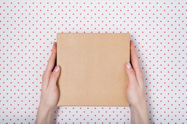 Square cardboard box in female hands. Top view, 