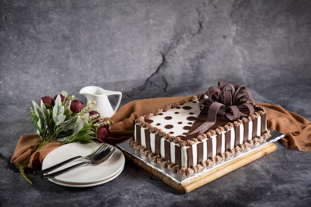 バラの花のスプーンとフォークが付いた正方形のチョコレート ケーキが、カフェで焼いた食べ物のナプキン側面図に分離されたボード上で提供されます