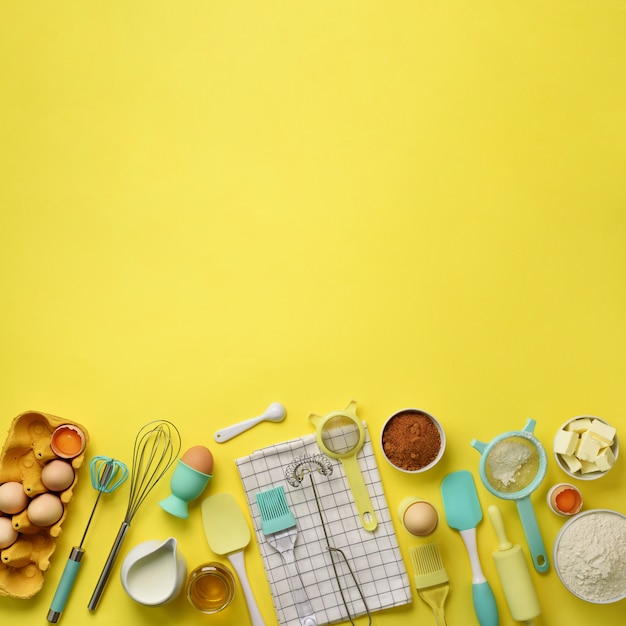 スクエアクロップベーキング成分 - バター、砂糖、小麦粉、卵、油、スプーン、麺棒、ブラシ、泡立て器、黄色の背景上のタオル。
