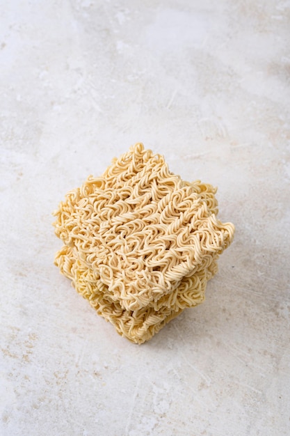 Square dry egg noodles in a briquette on a light beige stone marble background