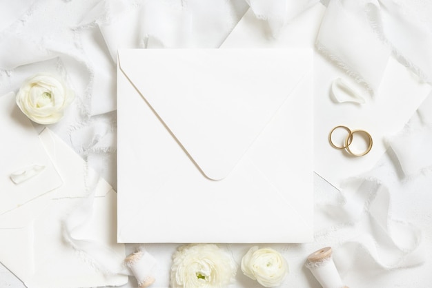 Square envelope near roses white silk ribbons and wedding rings top view wedding mockup