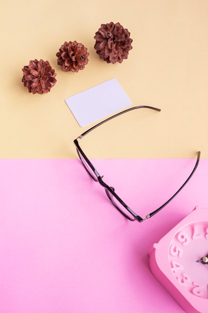 Square glasses, alarm clock, pine tree flowers on a pastel pink and pastel yellow background. Summer Concept, Minimal Concept