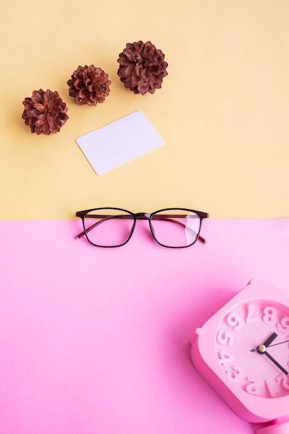 Square glasses, alarm clock, pine tree flowers on a pastel pink and pastel yellow background. Summer Concept, Minimal Concept