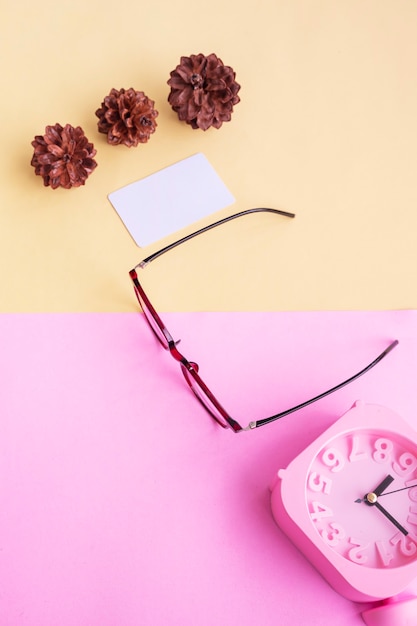 Square glasses, alarm clock, pine tree flowers on a pastel pink and pastel yellow background. Summer Concept, Minimal Concept