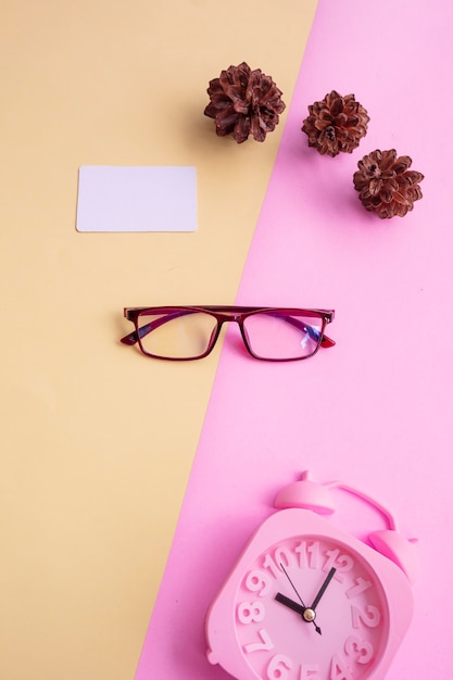 Photo square glasses on a pink and yellow background with additional accessories an alarm clock and pine tree flowers. minimal summer style