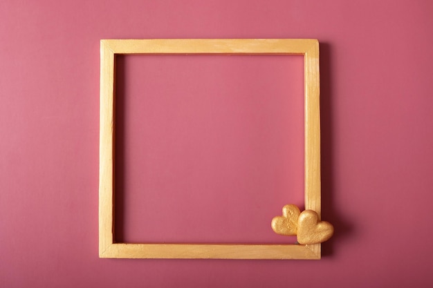 Square golden frame blank with golden hearts on red background Flat lay top view copy space