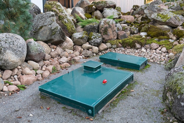 Square green metal cover of an autonomous septic tank with a warning lamp on the backyard