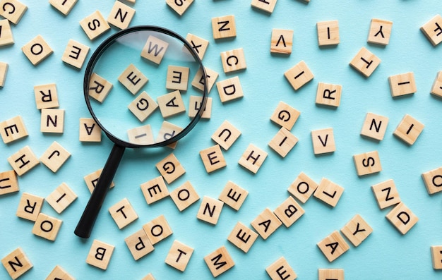 Photo square letter tiles with magnifying glass against blue background search for words and information