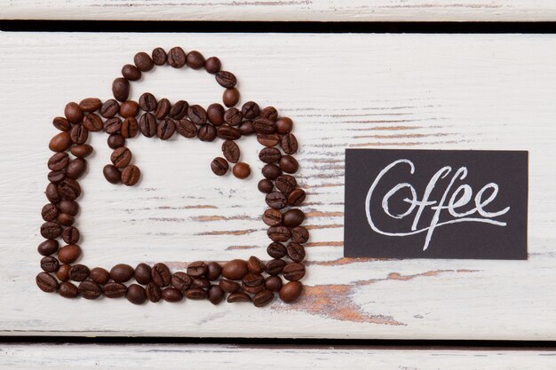 Square made of coffee beans on white wood. Abstract form looks like bag or satchel.