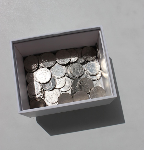 Photo square photo of cardboard money box with scattered ukrainian coins with different denomination