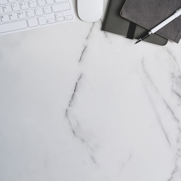 Square photo of workspace with keyboard, notebook, mouse and copy space on marble table.