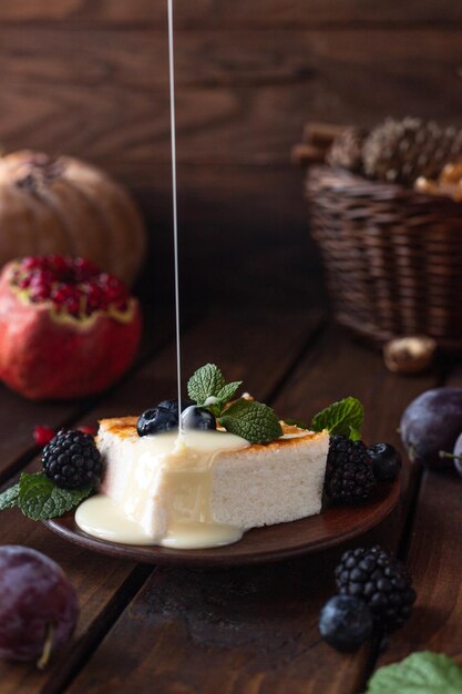 A square piece of cottage cheese casserole lies on a plate, decorated with berries and mint leaves. Condensed milk is poured on top of the omelet