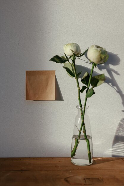 A square piece of paper is on a table with a vase of flowers