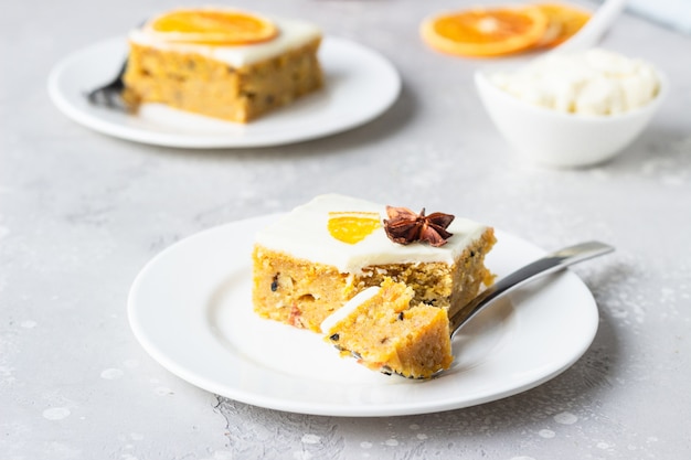 Square pieces of raw spiced carrot cake with orange, nuts and cream cheese frosting. 