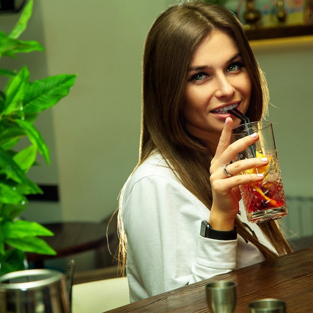Квадратный портрет молодой сексуальной женщины пьет коктейль за барным столом