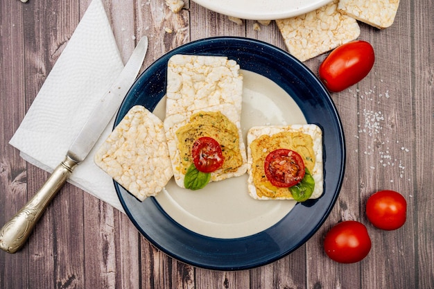 Square rice crackers with hummus and cherry tomatoes on a plate Tomatoes crackers on a rustic table and a platter with hummus Natural and healthy food concept