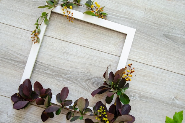 Square white wooden frame and copyspace framed by yellow flowers and green and burgundy leaves