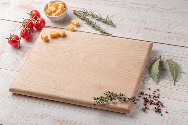 Square wooden cutting board with cherry tomatoes cheese and spices on a white background mockup with copy space for text side view