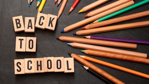 Square wooden letters with the phrase quotBack To Schoolquot written in English on a black chalkboard background and next to colored pencils