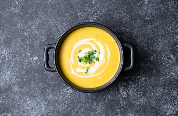 Squash vegan soup, creammy autumn soup in black bowl on dark background. Autumn foods.