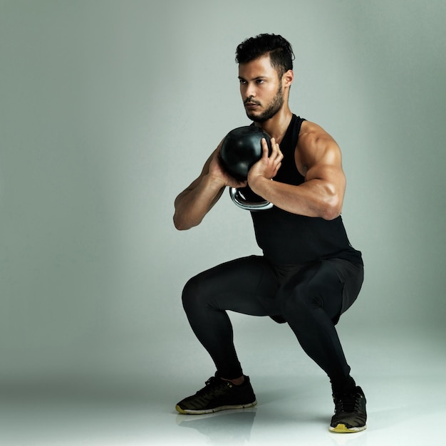 スクワット・アスリート (Kettlebell or Power for Muscle Health or Wellness on Grey Background) はフィットネス・トレーニングやバランスのためのウェイト・ワークアウトやバランス用のウェイト・エクササイズやモデルの強力なボディビルダーです