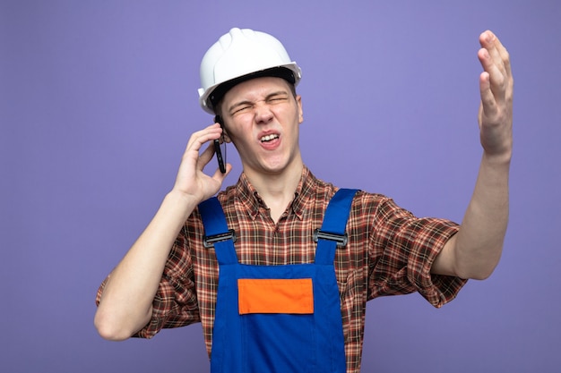 Squeamish young male builder wearing uniform speaks on phone 