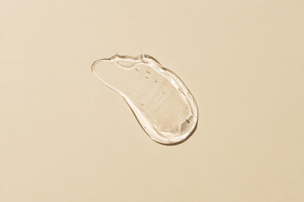 Squeezed cosmetic clear cream gel texture Iisolated on beige background Close up transparent serum drop smear